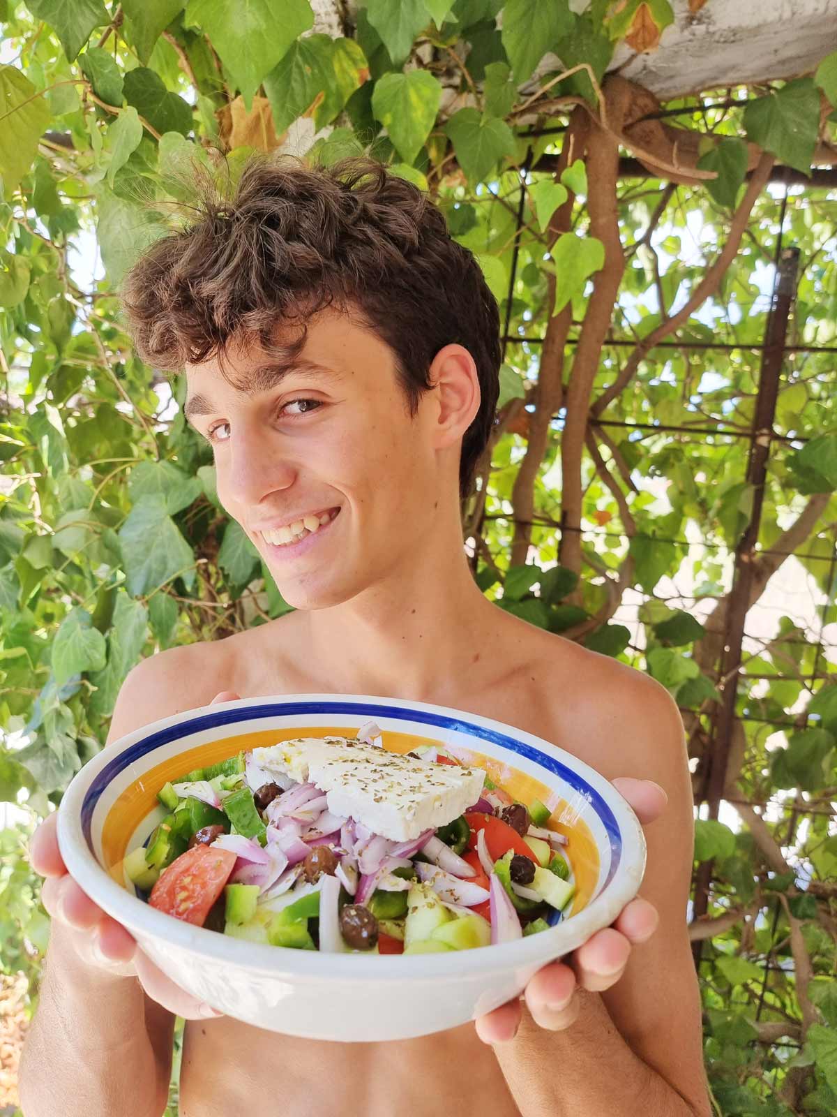 A smiling boy is holding a Greek salad.
