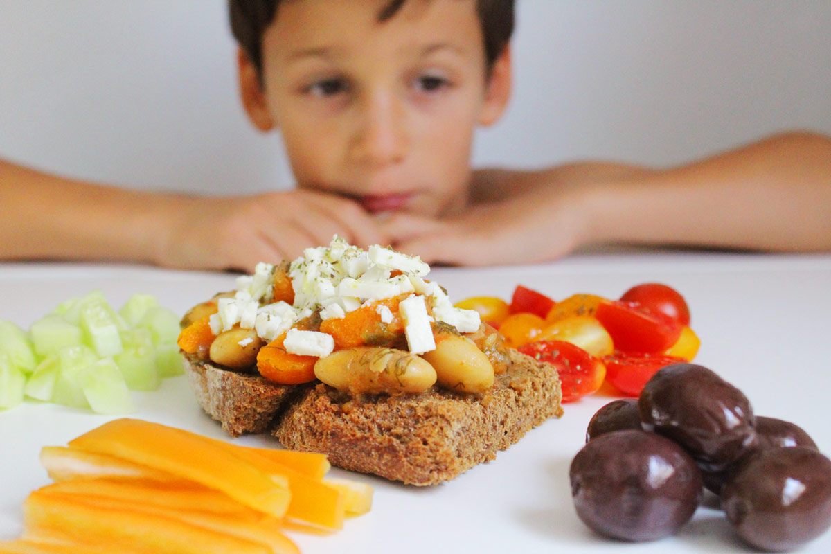 A boy is looking a platter with veggies and a giant beans bruschetta.