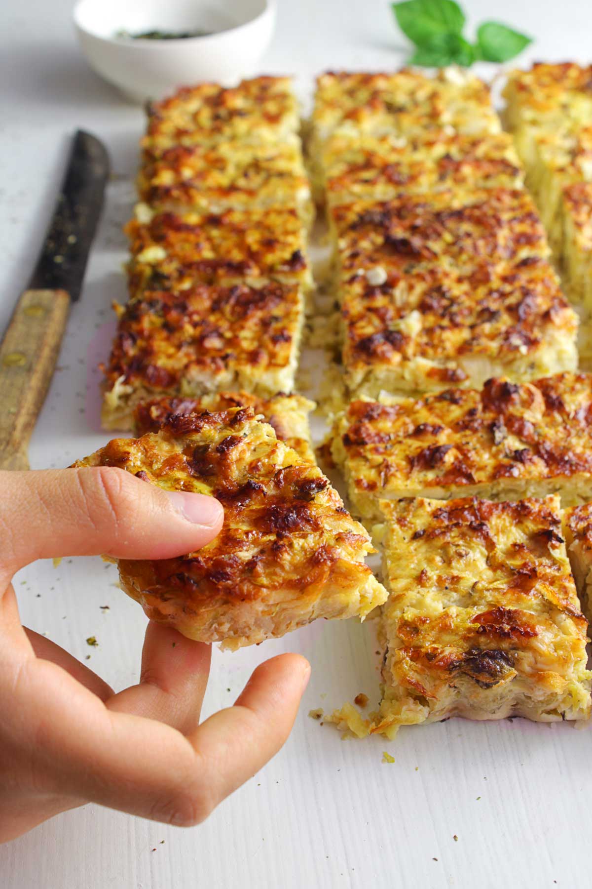 A hand is holding a piece of Greek zucchini pie.