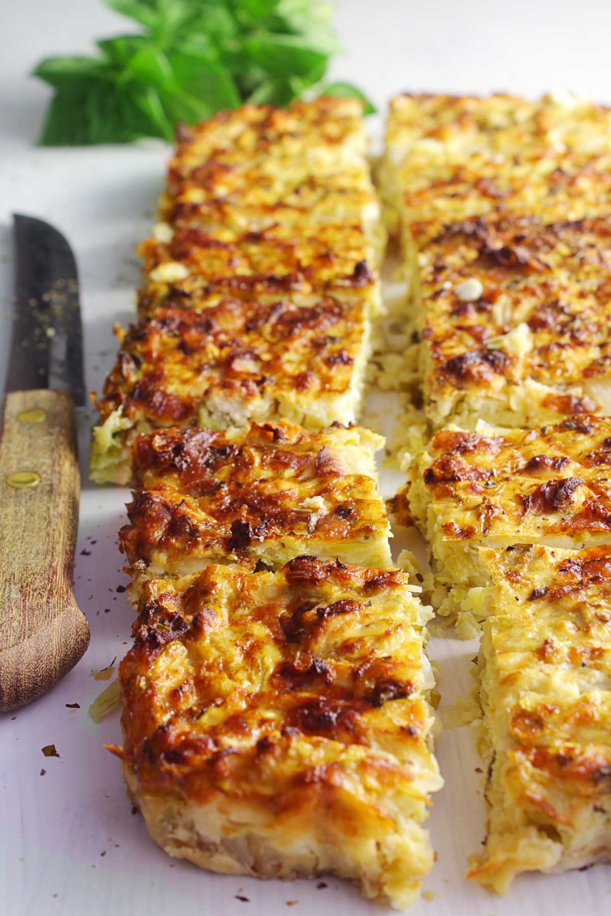 A Greek zucchini pie cut in pieces on a white board.