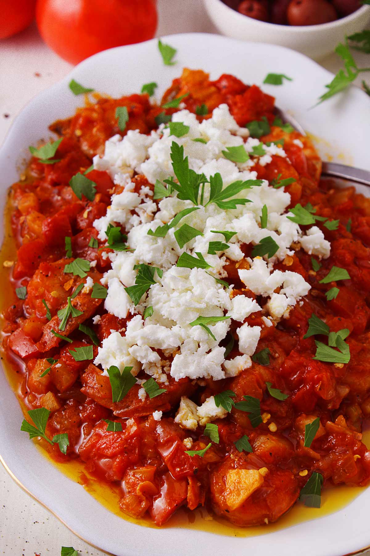A white platter with Greek shrimp saganaki topped with feta cheese and parsley.