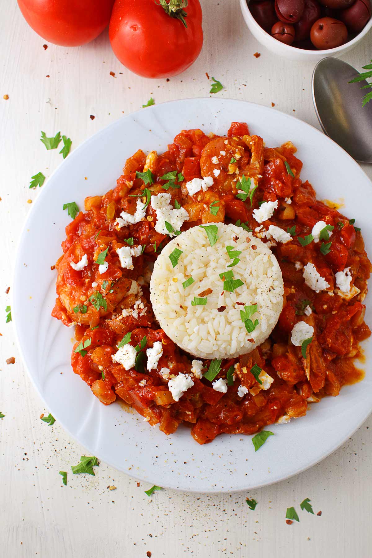 A white plate with Greek shrimp saganaki served with a ball of white rice.
