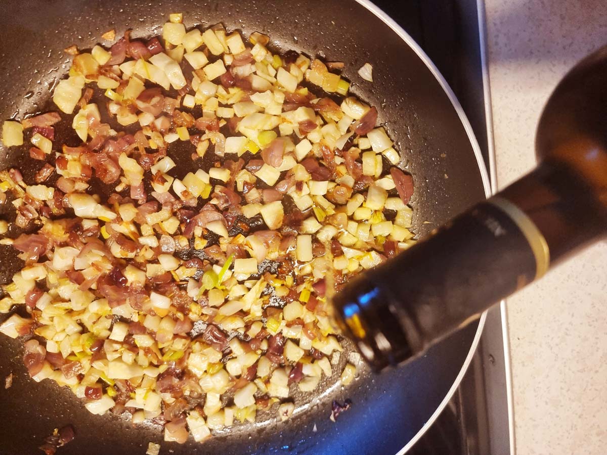 A skillet with vegetables and a bottle of wine is pouring wine over.