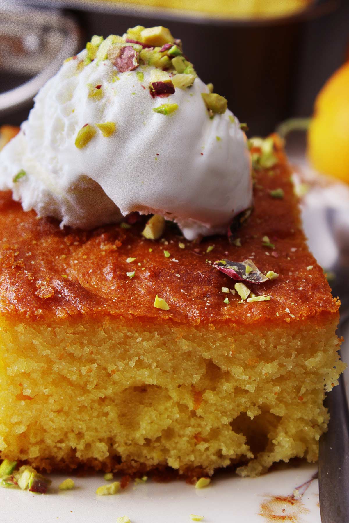 A close photo of a piece of Greek revani topped with vanilla ice cream and chopped pistachios.
