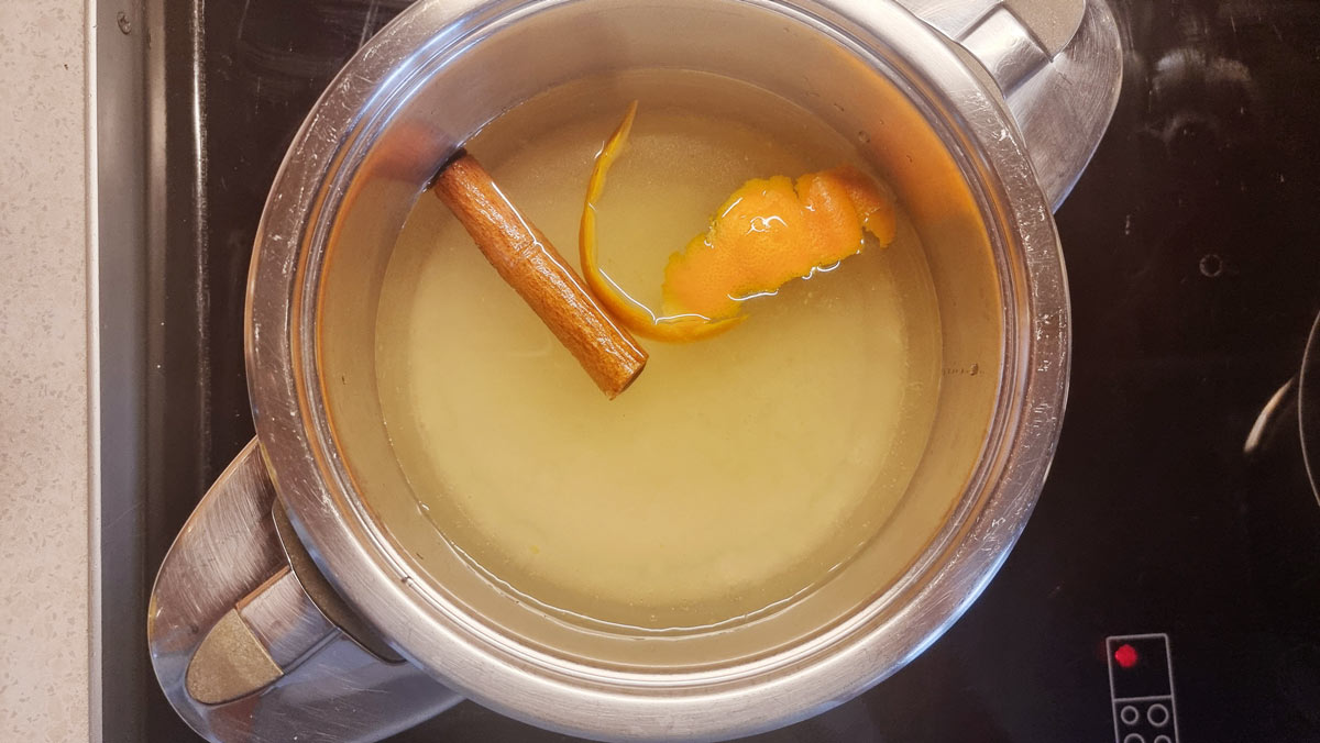 A small pan with ingredients like cinnamon, orange peels, sugar and water for making syrup.