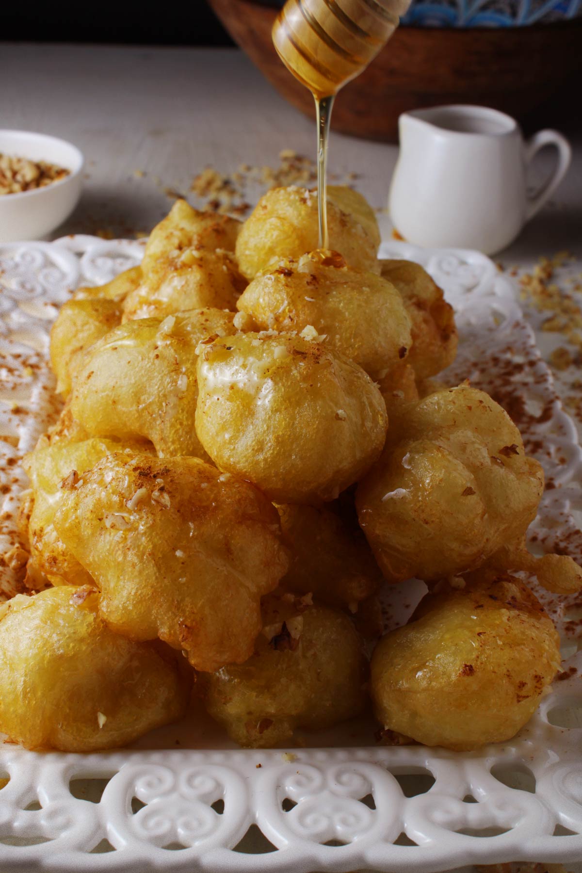 A platter with Greek donuts (loukoumades) and a honey spoon ovet it.