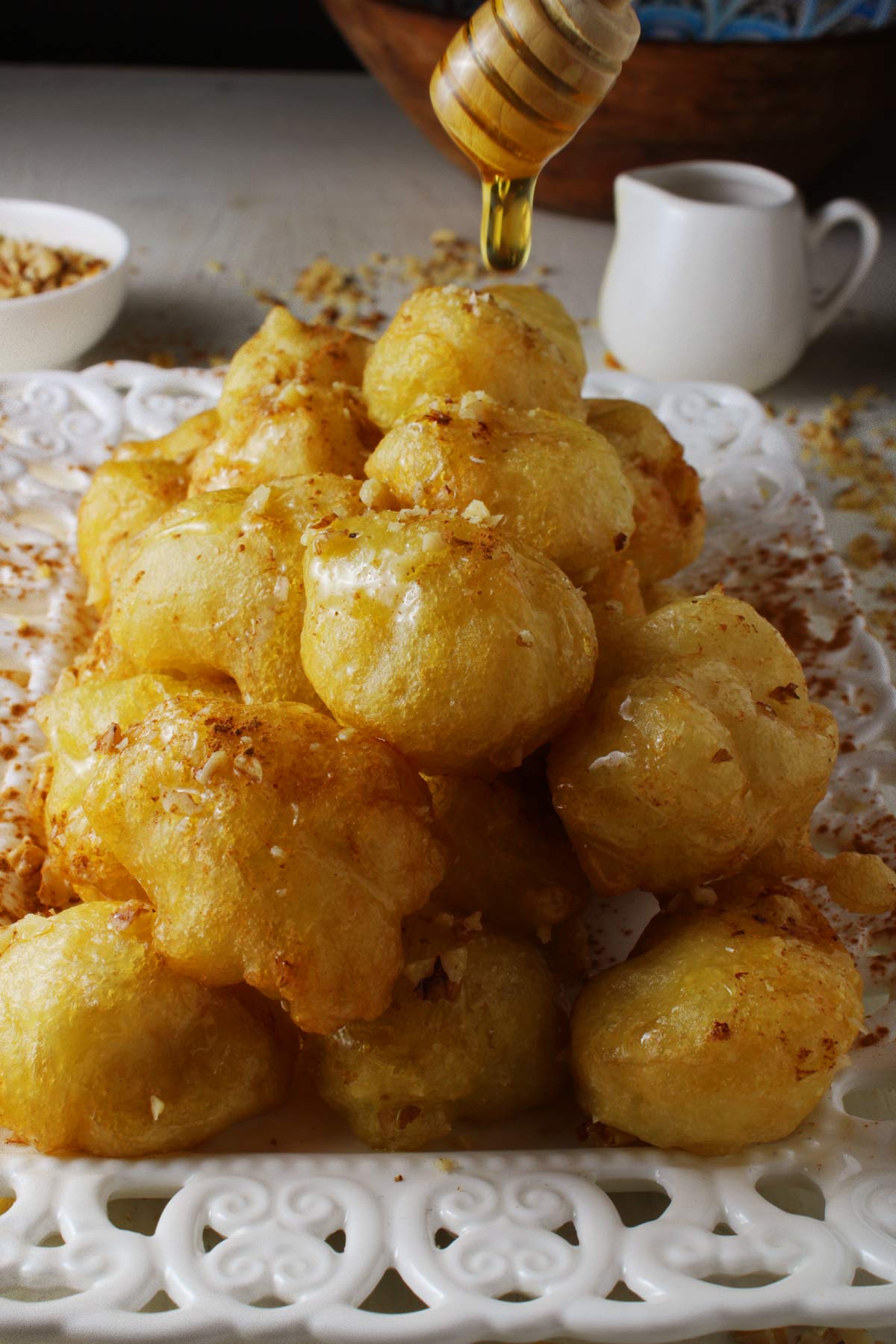 A white platter with Greek donuts (loukoumades) with honey spoon drizzling honey over them.