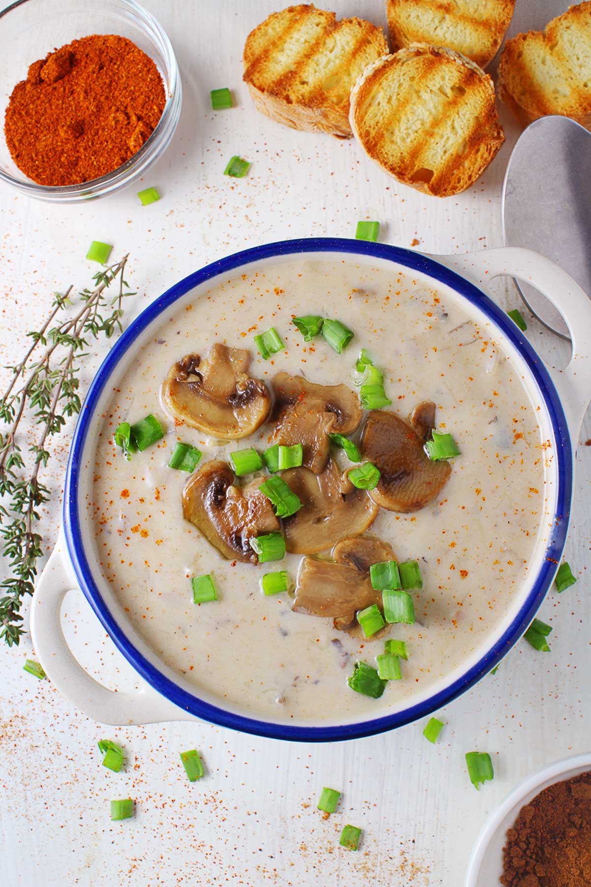 A bowl with a blue stripe with mushroom and leek soup topped with chopped spring onions.