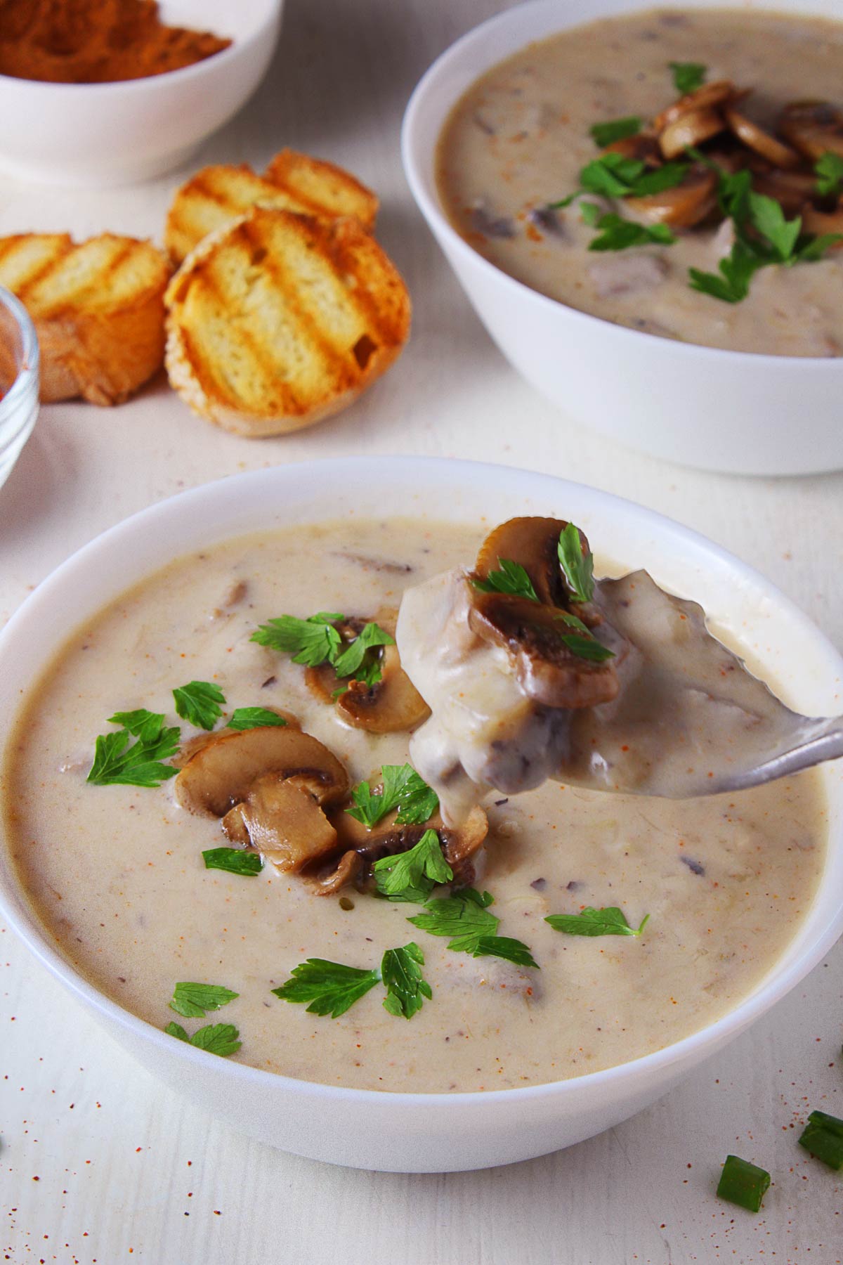 Two bowls of mushroom and leek soup and a spoonful over one of the bowls.