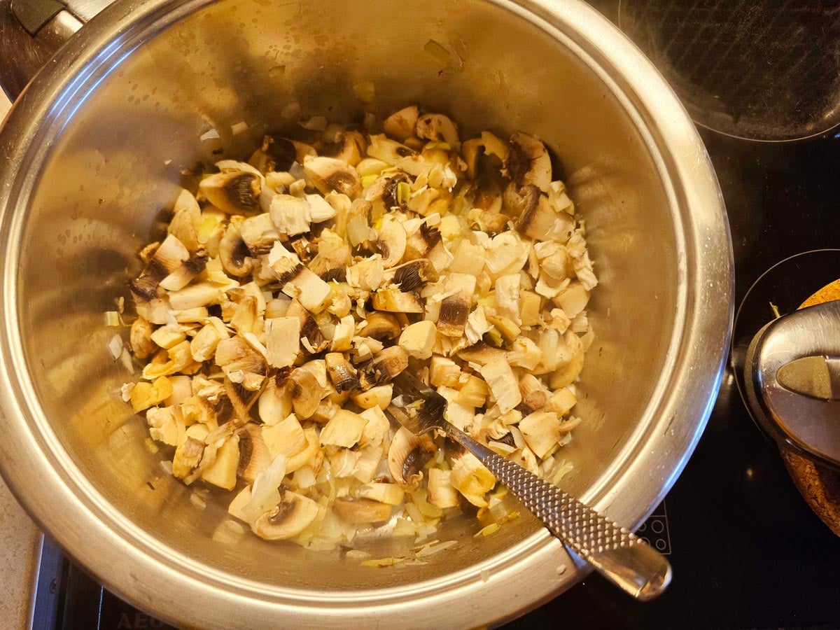 A big pot with mushrooms, chopped onions, leeks to make mushroom and leek soup.