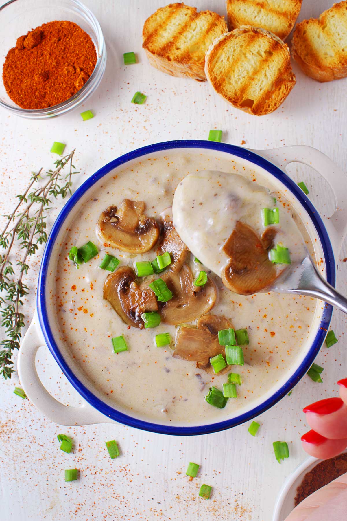 A hand holds a spoonful of mushroom and leek soup over a bowl.