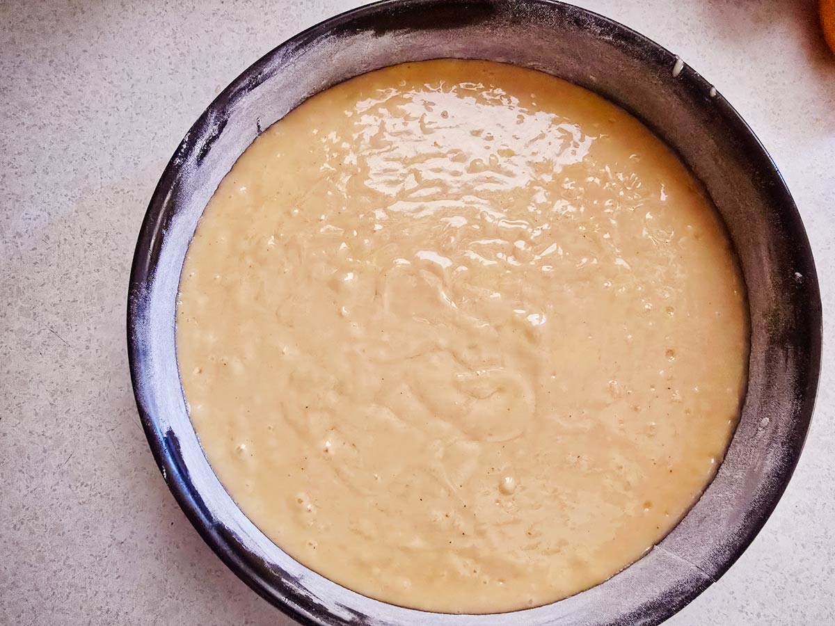 A black round baking pan with batter for Greek vegan cake ready for the oven.