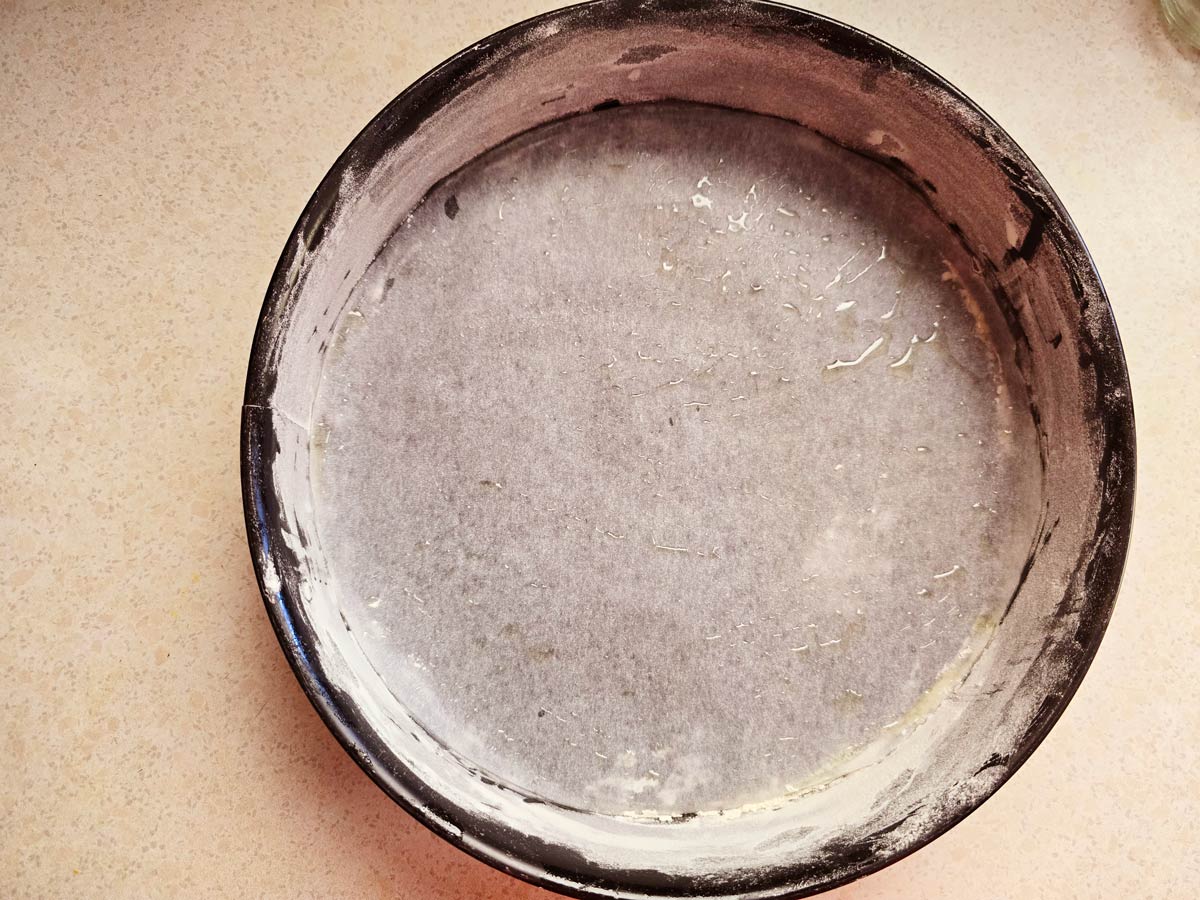 A black round baking pan lined with parchment paper and greased with oil and flour at the sides.